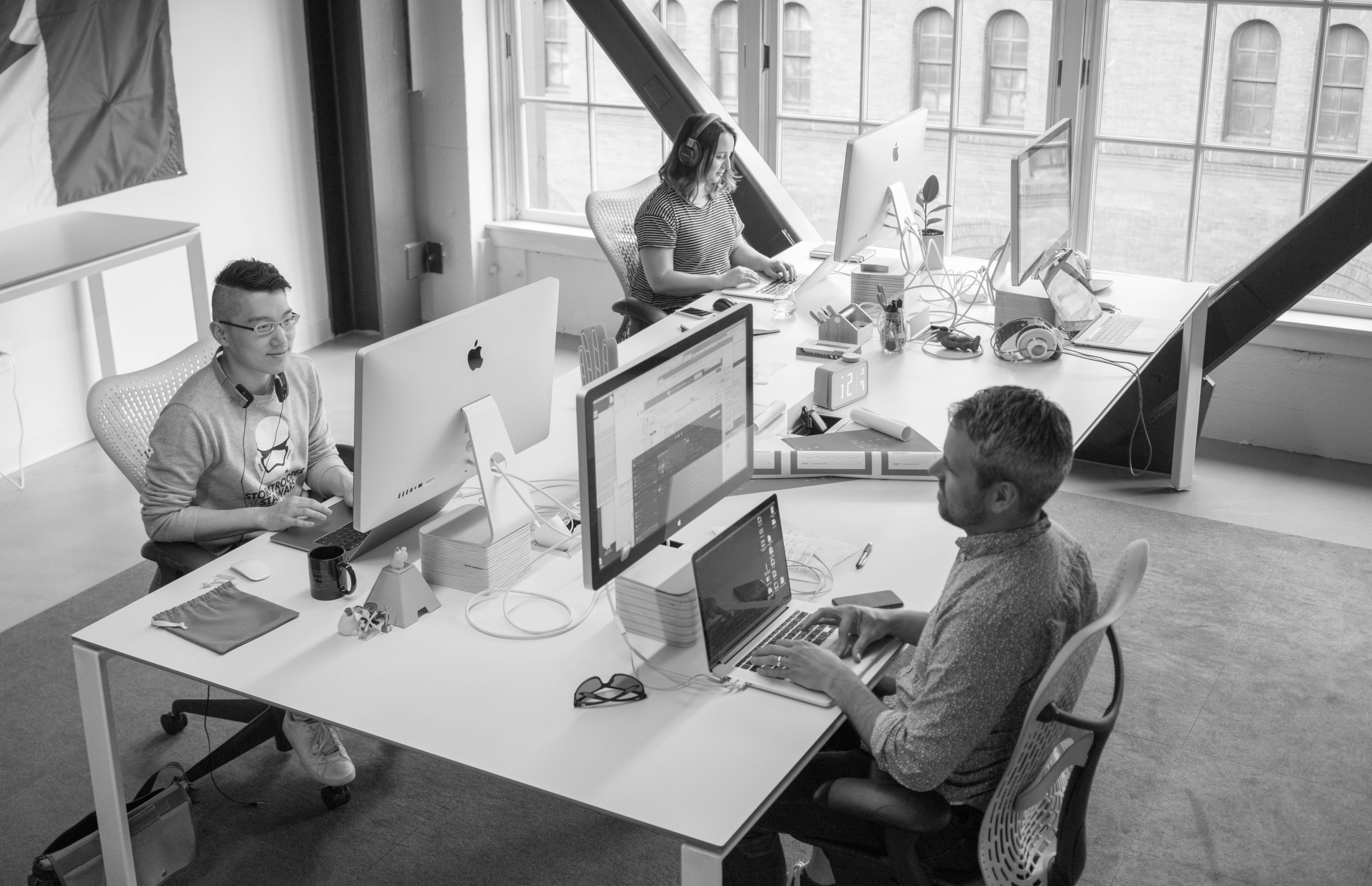 Black and white image of happy colleagues sitting at desk using computers working together